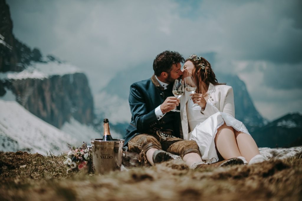 Couple Lying On The Mountain Grass Having A Toast For Two On Their Wedding Day To Celebrate