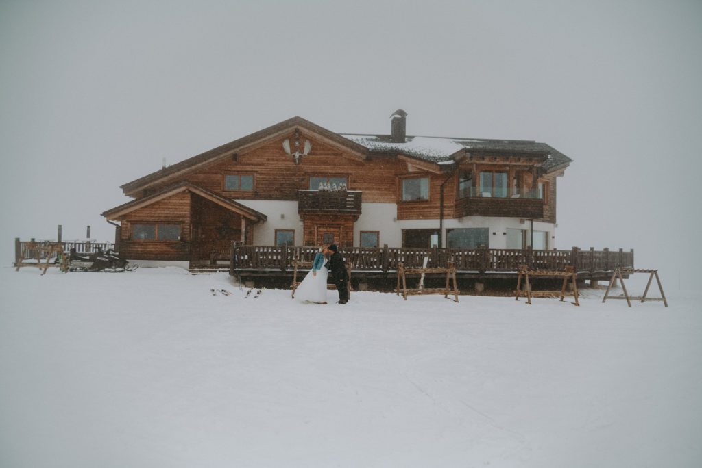 bride and groom kissing in a snowstorm in front of a mountain hut Cherz in the Dolomites