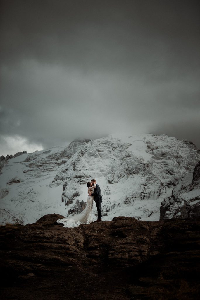 Pacchetti di Elopement sulle Dolomiti - Coppia epica di sposi che si baciano di fronte a una montagna innevata durante l'elopement.