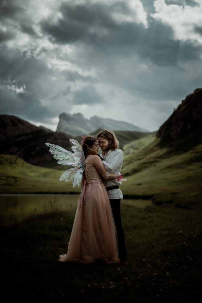 Hochzeitsfotograf Südtirol und Dolomiten - Verträumtes Fantasiepaar beim Kuscheln in den Dolomiten mit einem See im Hintergrund und dramatischem Himmel