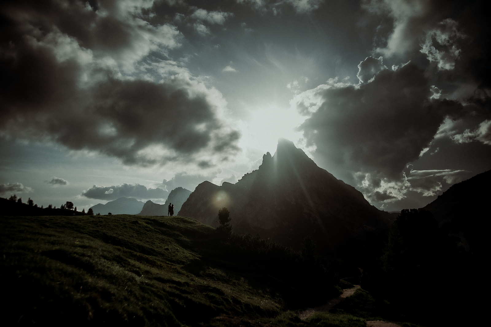 Sunset Engagement Session Dolomites - Couple looking at each other with mountain and sun in the background with dramatic light