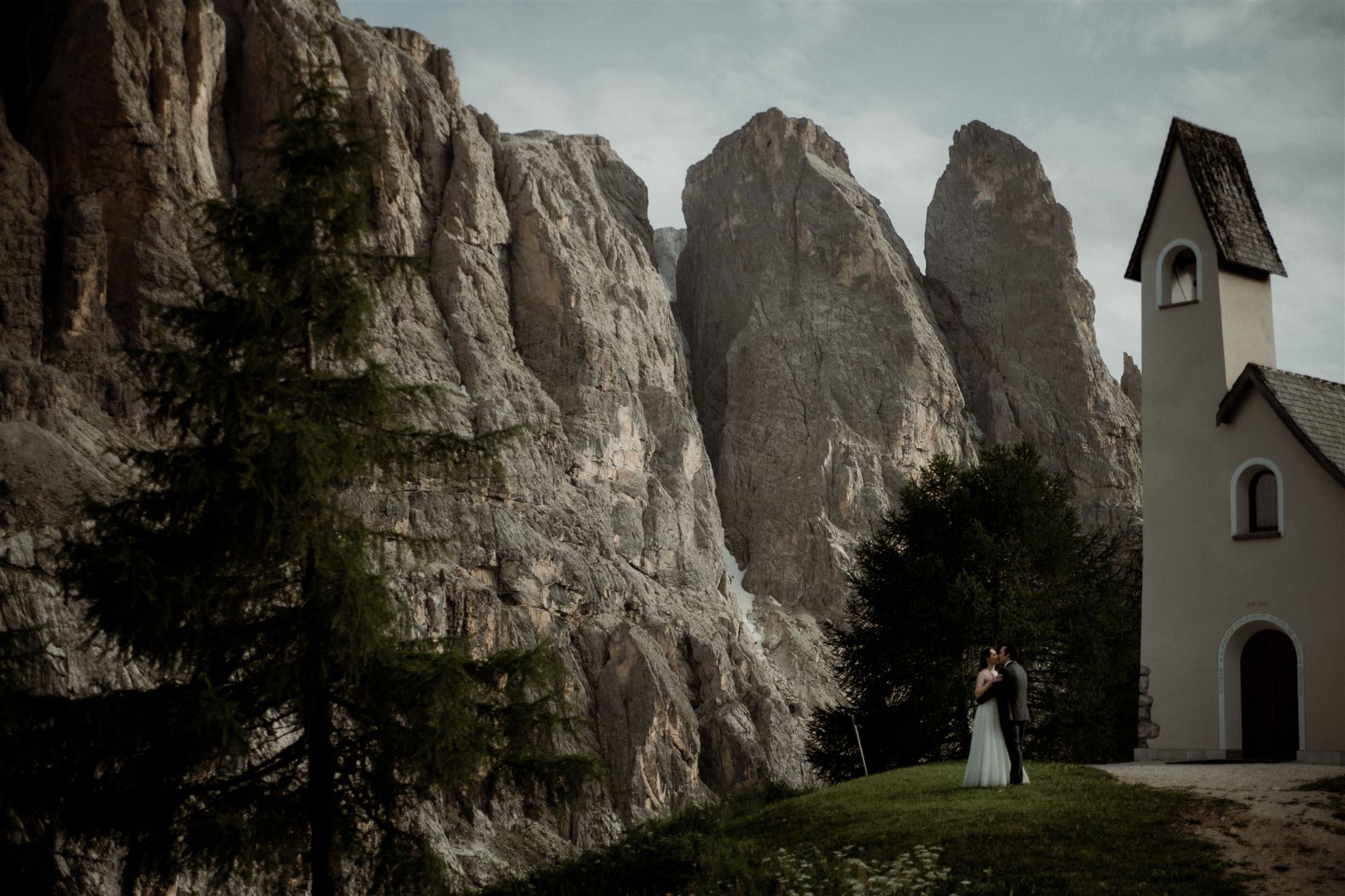Dolomites Elopement bride and groom kissing in front of a small chapel with huge dolomites mountains in the background